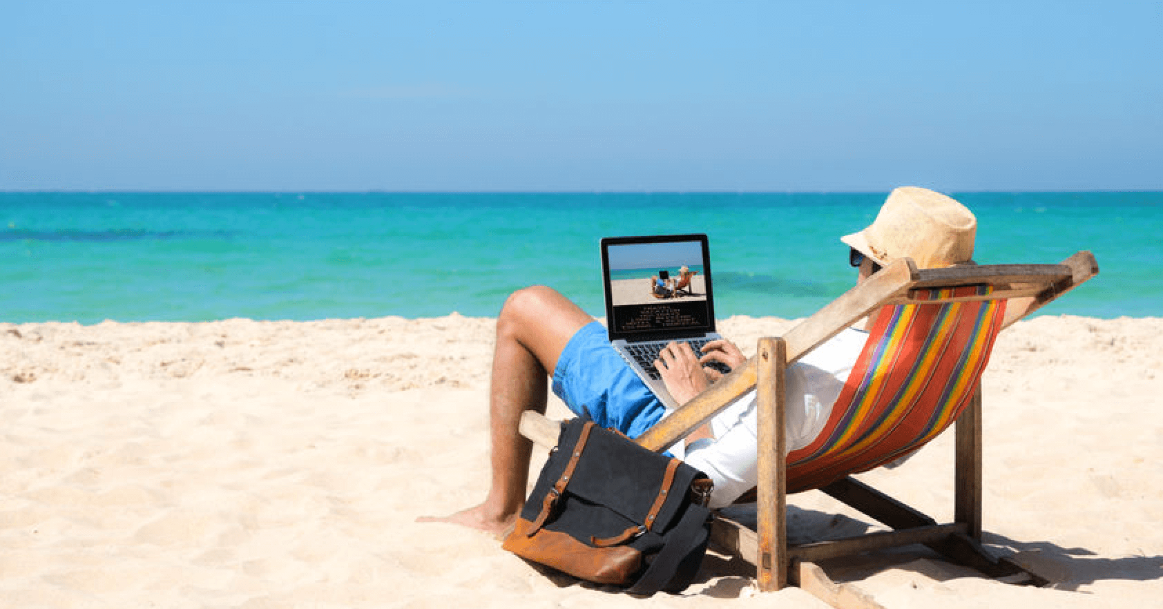 Homme allonge dans un transat sur la plage avec un ordinateur sur les genoux